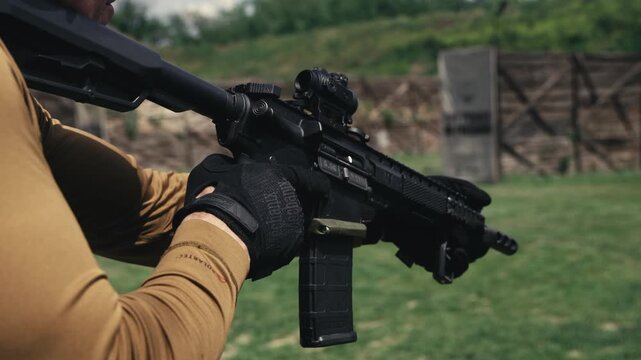 Shooter wearing protective gloves aims a modern rifle with optical sight at an outdoor shooting range.