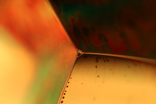 Fluid film plane intersection with micro droplet vertex node and warm amber glow
 Description: A low-key macro perspective capturing the geometric intersection of liquid film planes 