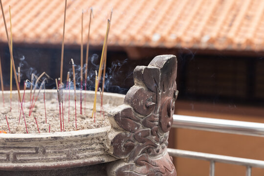 Burning incense sticks fill an ornate temple incense burner with thin trails of smoke evoking calm, devotion and tradition.