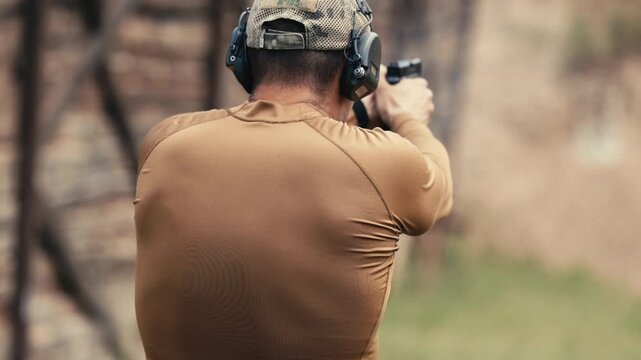 Man wearing hearing protection shoots a handgun at a target on an outdoor shooting range.