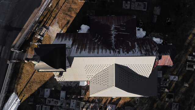 Aerial view of the church roof in Mouthe, featuring textured metal roofing, a bell tower, and surrounding cemetery grounds with snow under golden hour light, Mouthe, Bourgogne-Franche-Comte, France.