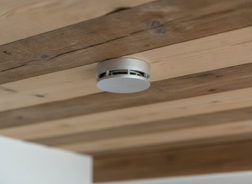 Modern smoke detector mounted on a rustic wooden ceiling, providing essential home safety and fire protection in a residential setting.