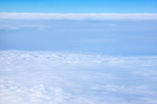 An aerial view from an airplane window looking out over a thick, rolling layer of low-level clouds beneath a clear blue sky. A vast sheet of white, textured clouds, typical of a low cloud layer. 