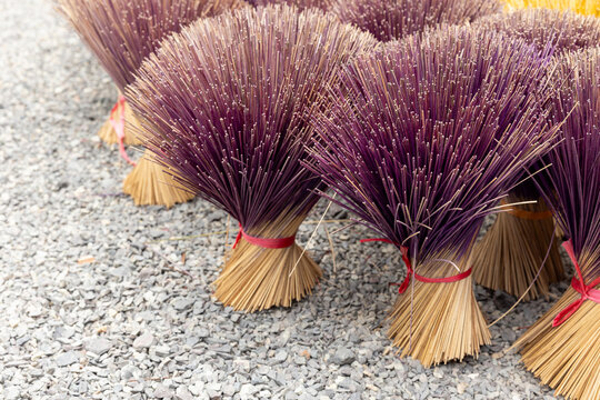 Purple incense sticks bundled and tied with red ribbons stand upright on a concrete floor to dry, highlighting, handmade craft and traditional ritual objects
