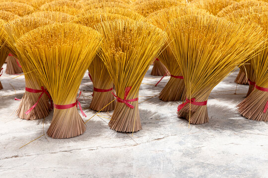 Bright yellow incense sticks bundled and tied with red ribbons stand upright on a concrete floor to dry, highlighting repetitive texture, handmade craft and traditional ritual objects with warm tones