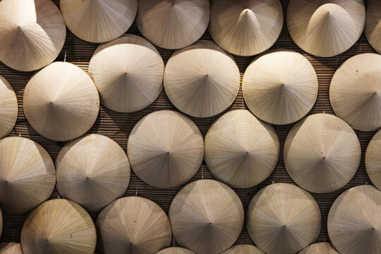 A display of traditional Vietnamese conical hats Non La arranged in a repeating grid on a bamboo background, highlighting texture, craftsmanship and cultural decor in neutral warm tones