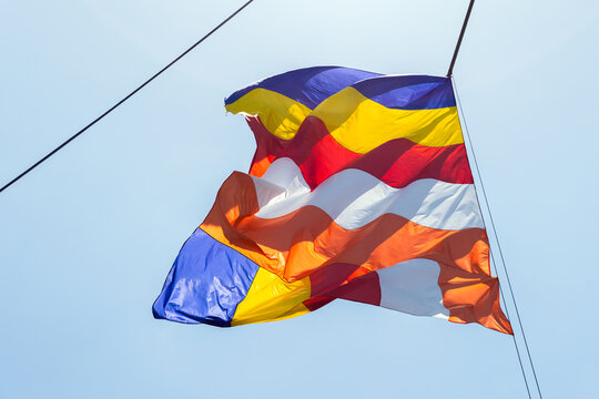 Colorful Buddhist flag with vertical stripes waving on a rope against clear blue sky. Image evokes spirituality, peace, cultural tradition, ceremony and unity at a temple event