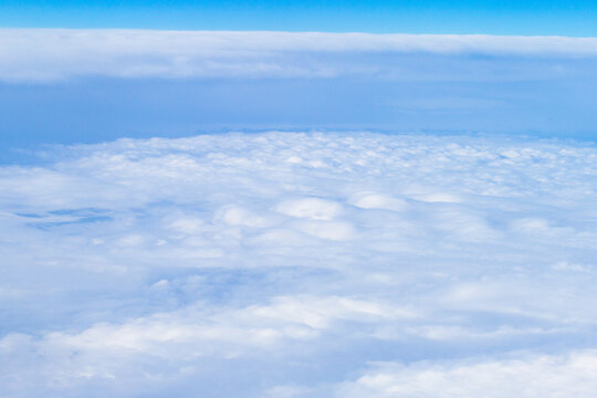 An aerial view from an airplane window looking out over a thick, rolling layer of low-level clouds beneath a clear blue sky. A vast sheet of white, textured clouds, typical of a low cloud layer. 