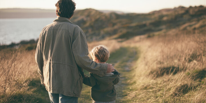 father and young son walking together outdoors along coastal path back view warm golden hour sunlight countryside sunset path nature family bonding parenthood fatherhood concept countryside stroll