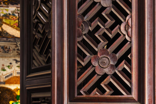 Ornate carved wooden lattice screen panel from Asian architecture featuring floral medallions and geometric fretwork, warm mahogany tones and fine handcraft details for heritage and interior design