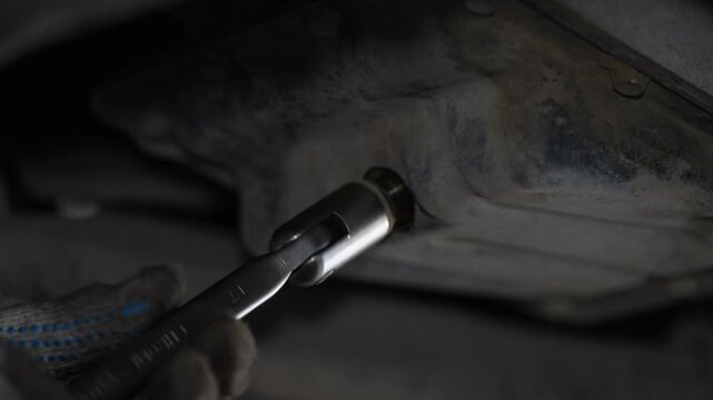 Mechanic loosening a car engine oil pan drain plug bolt.