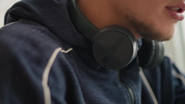 Close up of man wearing black headphones around his neck and speaking showing slight mouth movements. subject is dressed in dark blue zip up hoodie with white stripes on sleeves focusing