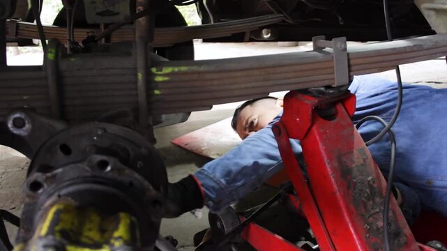 A Latino mechanic lies down while checking the wheel pulleys under a bus inside a mechanic's shop in Neiva, Huila, Colombia. Concept of automotive industry