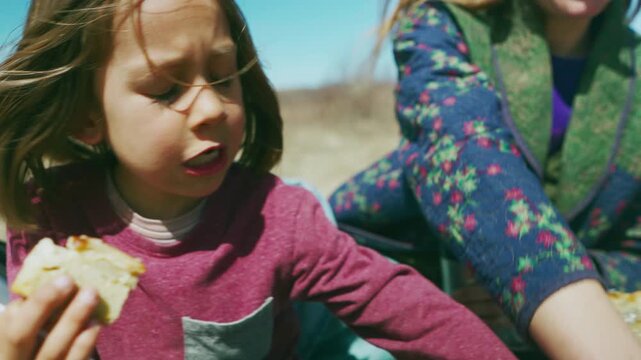 Boy eating sandwich while mother pours from thermos during prairie picnic