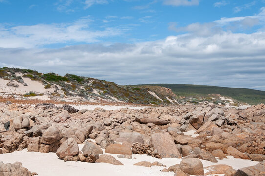 Rugged Western Australian coast featuring weathered rocks, pale sand and low coastal scrub under dramatic clouds