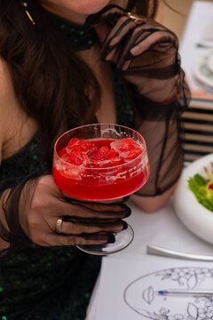 Woman holds a cocktail with strawberries while sitting at a table with food