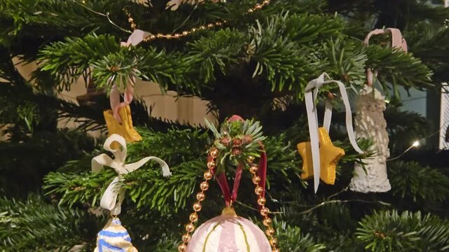 Colorful paper flags hang from a decorated Christmas tree. Festive ornaments dangle among green pine branches. Beaded garlands add charm to the holiday scene