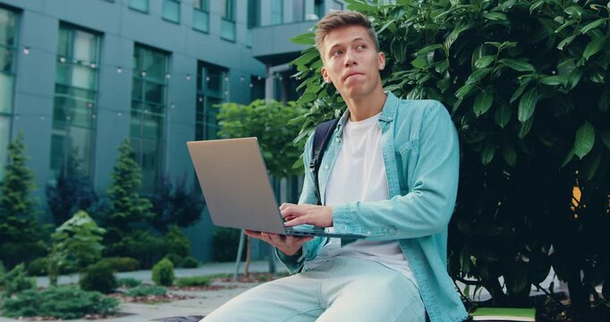 Portrait of a student man working on a laptop outdoors, smiling with confidence as he types and analyzes data on the screen.