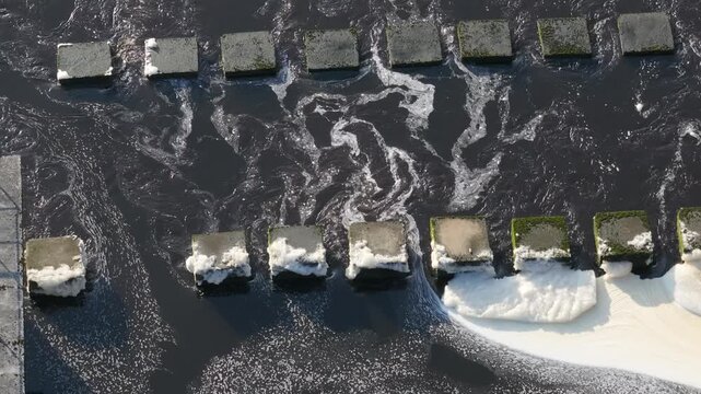 Aerial view of water pollution with foam and industrial concrete blocks in a dark river.