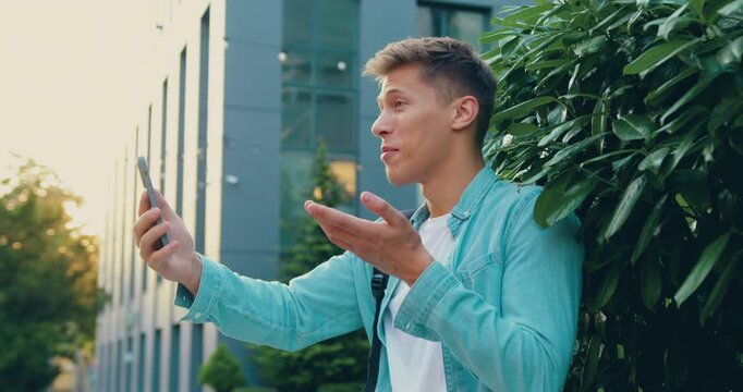 Close up of student sman using smartphone for a video call while standing outside a modern glass office building, technology and corporate lifestyle.