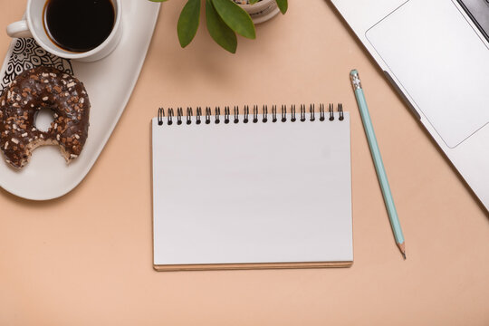 Coffee and donut on a table with empty notebook and laptop ready for work and ideas