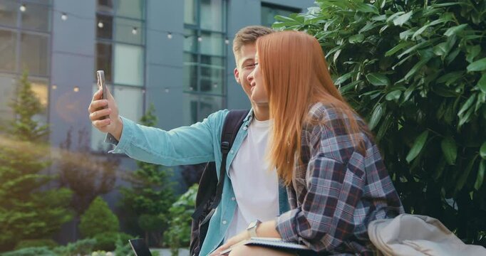 Man and woman students studying online, using smartphone, makes of distance learning walking by university campus. Male and female freelancer working on outside during break time