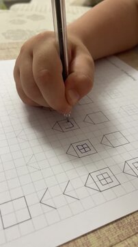 Child's hand with a pen draws geometric shapes on graph paper, emphasizing a house shape with a window, highlighting the learning and creativity in a well-lit indoor environment. High quality 4k