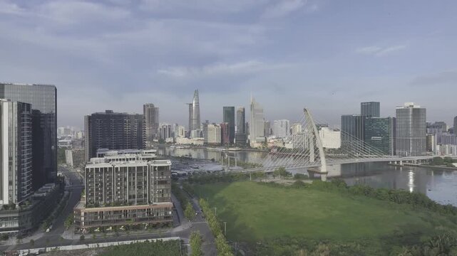 Aerial drone view of Thu Thiem, Saigon River and Ba Son Bridge, with Bitexco Financial Tower in Ho Chi Minh City, Vietnam, illuminated by bright sunlight over the modern urban skyline.