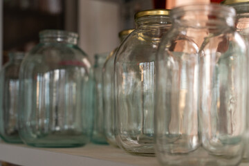 Empty clear glass jars of different sizes on a shelf prepared for home canning, food preservation,...