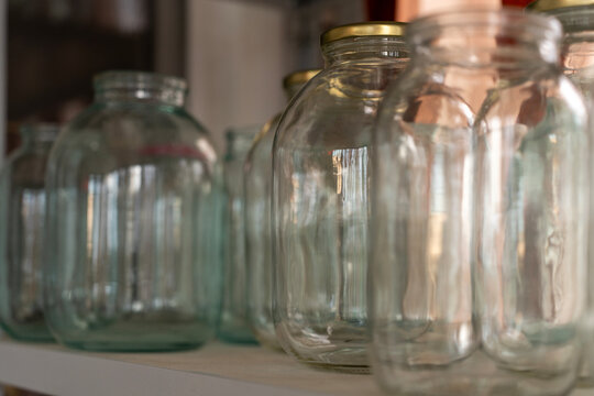 Empty clear glass jars of different sizes on a shelf prepared for home canning, food preservation, and pantry storage.