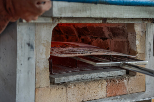 Enamel metal plate loaded into hot muffle kiln for thermal firing during craft manufacturing process in artisan workshop.