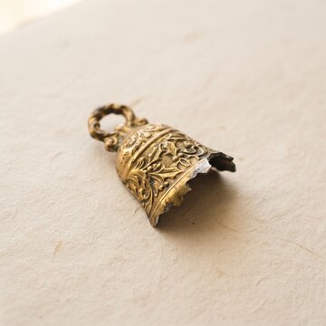 Antique broken brass bell fragment with engraved floral holly details resting on textured cream paper.