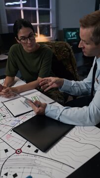 Caucasian male officer and female specialist discussing strategy over map in command center, vertical. Footage ideal for national security, defense technology, or tactical planning videos