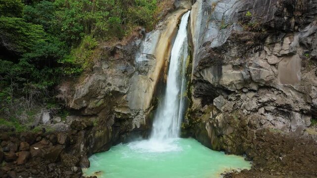 Aerial view of Mangku Sakti waterfall falling into turquoise sulfur pool in Rinjani rainforest Lombok