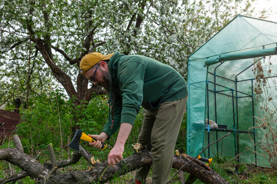 A man is chopping the trunk of a fallen tree.