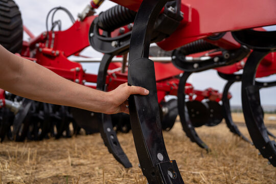 Farmer hand inspecting cast metal ripper tooth of agricultural subsoiler machine on dry wheat stubble field before deep tillage work.