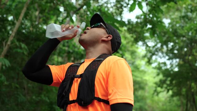 Man drinking water during a trail run in a mountain forest. Outdoor fitness, hydration, endurance and personal challenge while pursuing health goals and an active lifestyle.
