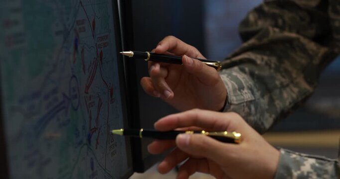 Close-up of military personnel pointing with pens at a tactical map on a screen during a planning briefing.