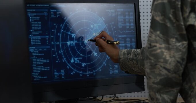 Military operator in camouflage studies a glowing digital radar display, using a stylus to analyze maps, signals, and tactical data in a dark command room.