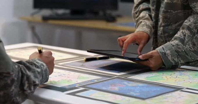 Military personnel in camouflage uniforms review maps and a tablet together at a planning table, teamwork, strategy, and mission preparation.