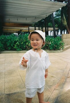 Joyful toddler in a sun hat and white outfit reaching out