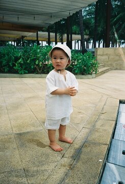 Young child in white outfit and hat standing outdoors