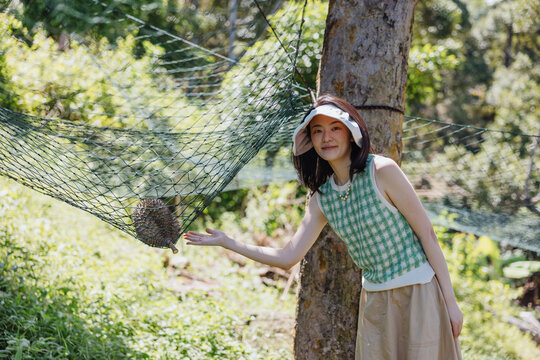 Woman presenting durian caught in protective harvest net at orchard