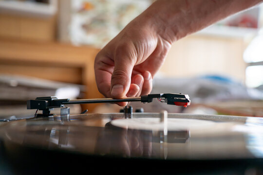 Male hand placing tonearm needle cartridge onto rotating black vinyl record on turntable player, illustrating analog sound reproduction and audio hobby.