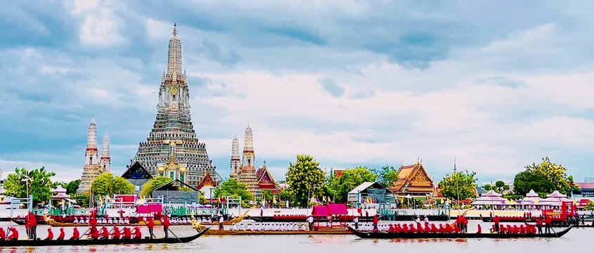 A golden Thai royal barge processional rowing past the iconic Wat Arun temple on the Chao Phraya River in Bangkok, Thailand during a traditional cultural ceremony under a bright daylight sky.