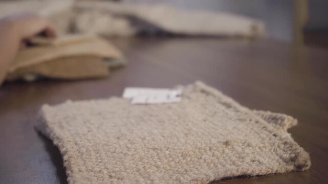 Close up hands sort and stack rustic woven fabric samples on a wooden table, comparing texture and color in warm natural light.