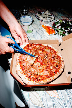 a man cuts a delivery pizza into slices beside a fresh meal