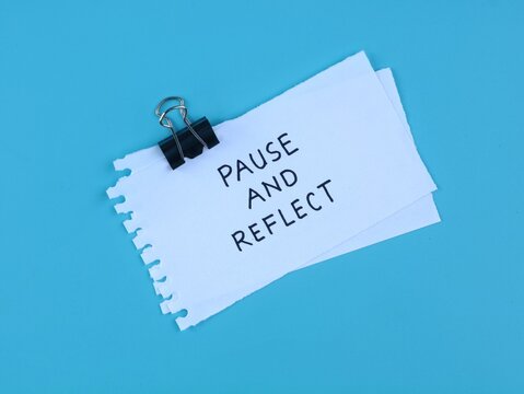 Pause and reflect text handwriten on white note paper clipped with binder clip over blue background. Concept for mindfulness, business evaluation, mental health, self care, and strategy