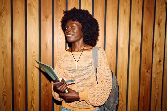 Student stands next to a wooden wall and smiles