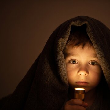 Close-Up of Scared Boy Peeking from Beneath Blanket with Flashlight Glow